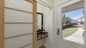 Un couloir doté d’une porte coulissante, d’une petite étagère ornée d’objets décoratifs et donnant sur une rue résidentielle.