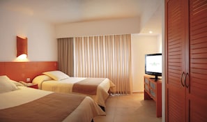 A hotel room with two beds, a TV on a wooden cabinet, and a curtain.