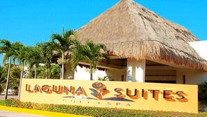 A sign for Laguna Suites with a thatched roof structure and palm trees in the background. - Laguna Suite (Cancun)