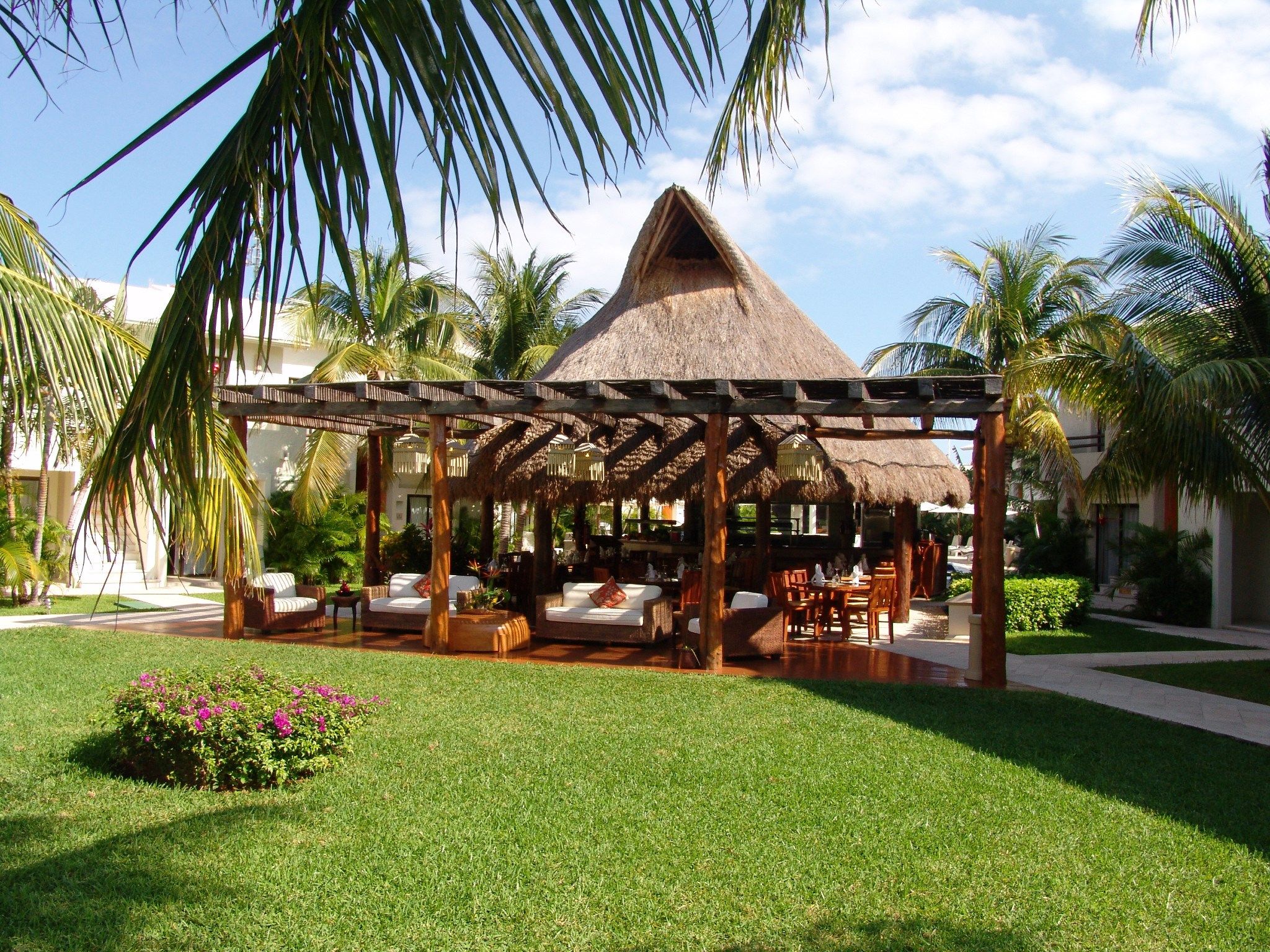 A resort with a thatched-roof gazebo, outdoor seating, and palm trees.