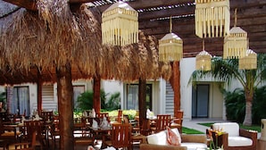 An outdoor seating area with wicker furniture, a round table with a plant, and hanging lanterns. - Laguna Suite (Cancun)