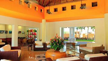 Un hall espacioso con muebles de mimbre, un arreglo floral central y vistas al exterior.
