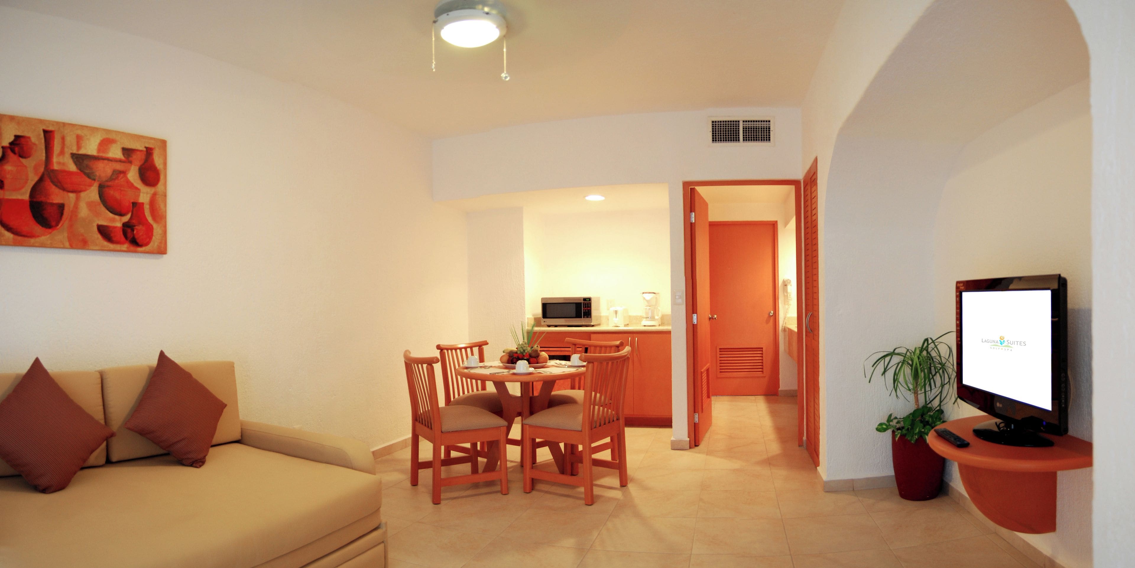 Una sala de estar con un sofá, una mesa de comedor con sillas, una zona de cocina y un televisor.