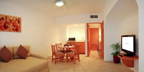 A living room with a sofa, a dining table with chairs, a kitchen area, and a television.