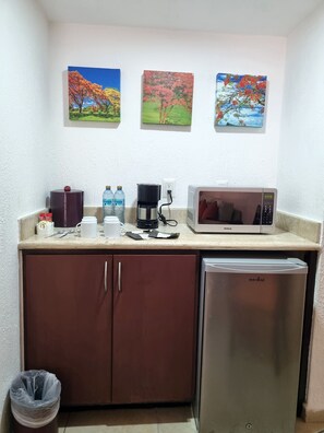 Una kitchenette equipada con microondas, refrigerador, cafetera y botellas de agua.