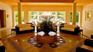 A spacious lobby with two sofas facing a central coffee table, a large window offering a view of a pool and palm trees, and ceiling fans. - Laguna Suite (Cancun)