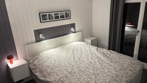 Une chambre à coucher comprenant un lit, des tables de chevet, une commode, une photo encadrée et une porte coulissante donnant sur une vue agréable.