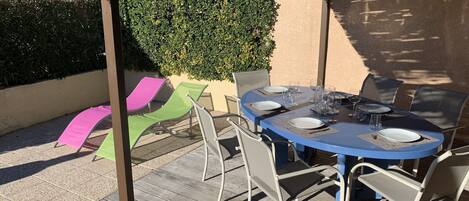 Un patio exterior techado con una mesa redonda dispuesta para comer, rodeado de sillas.