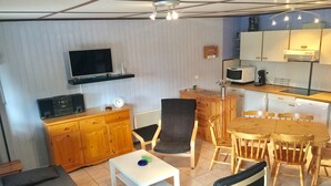 Un espace de vie compact comprenant un canapé, une table à manger avec des chaises, un coin cuisine avec un four à micro-ondes et un téléviseur posé sur une étagère.