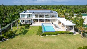 A modern two-story house with a large swimming pool, surrounded by lush greenery and a clear view of the ocean. - Family Friendly Villa inside Punta Cana Resort&Club with maid included! (Punta Cana)