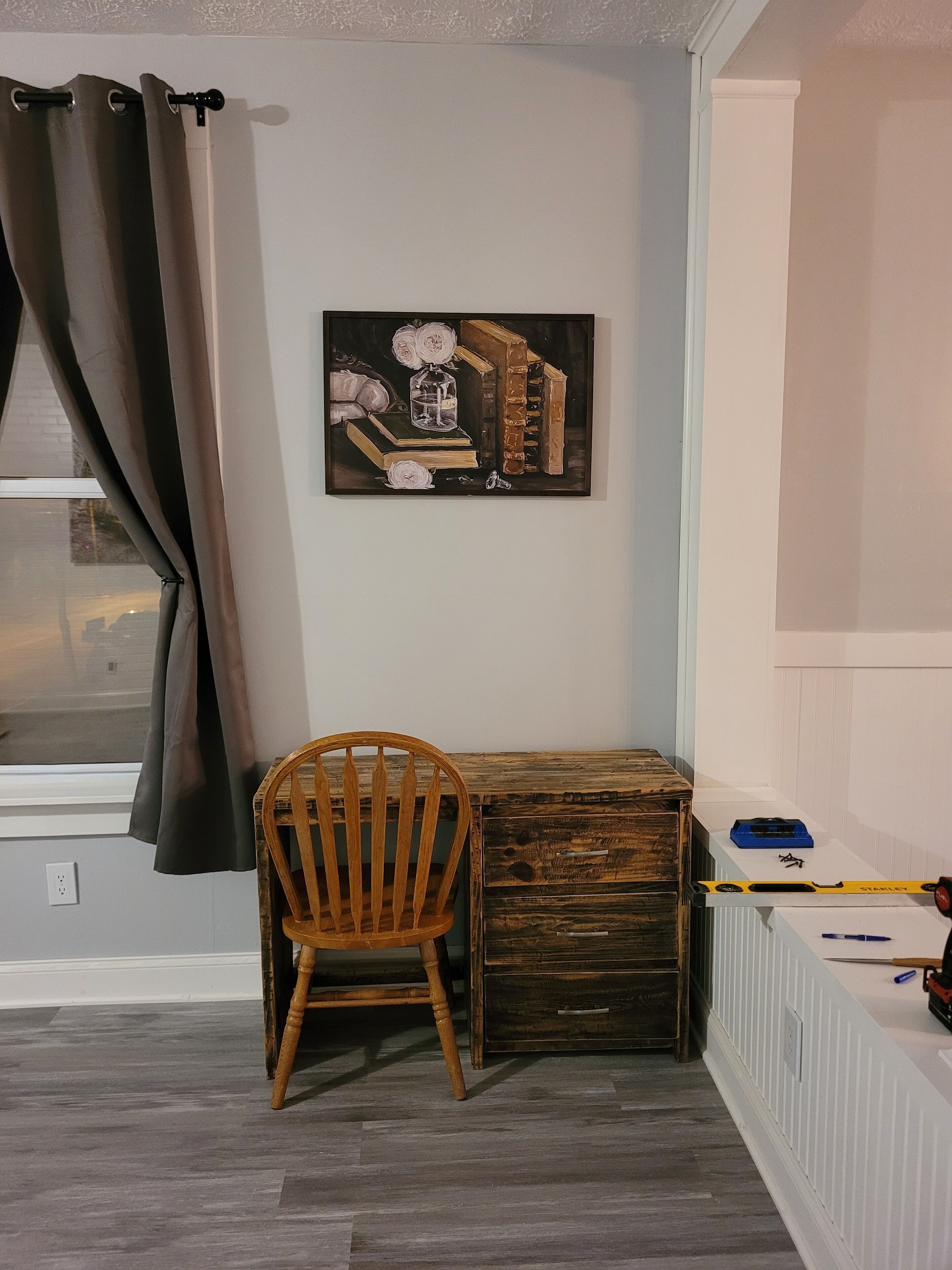 Een kamer met een houten bureau, een stoel, een radiator en een schilderij aan de muur.