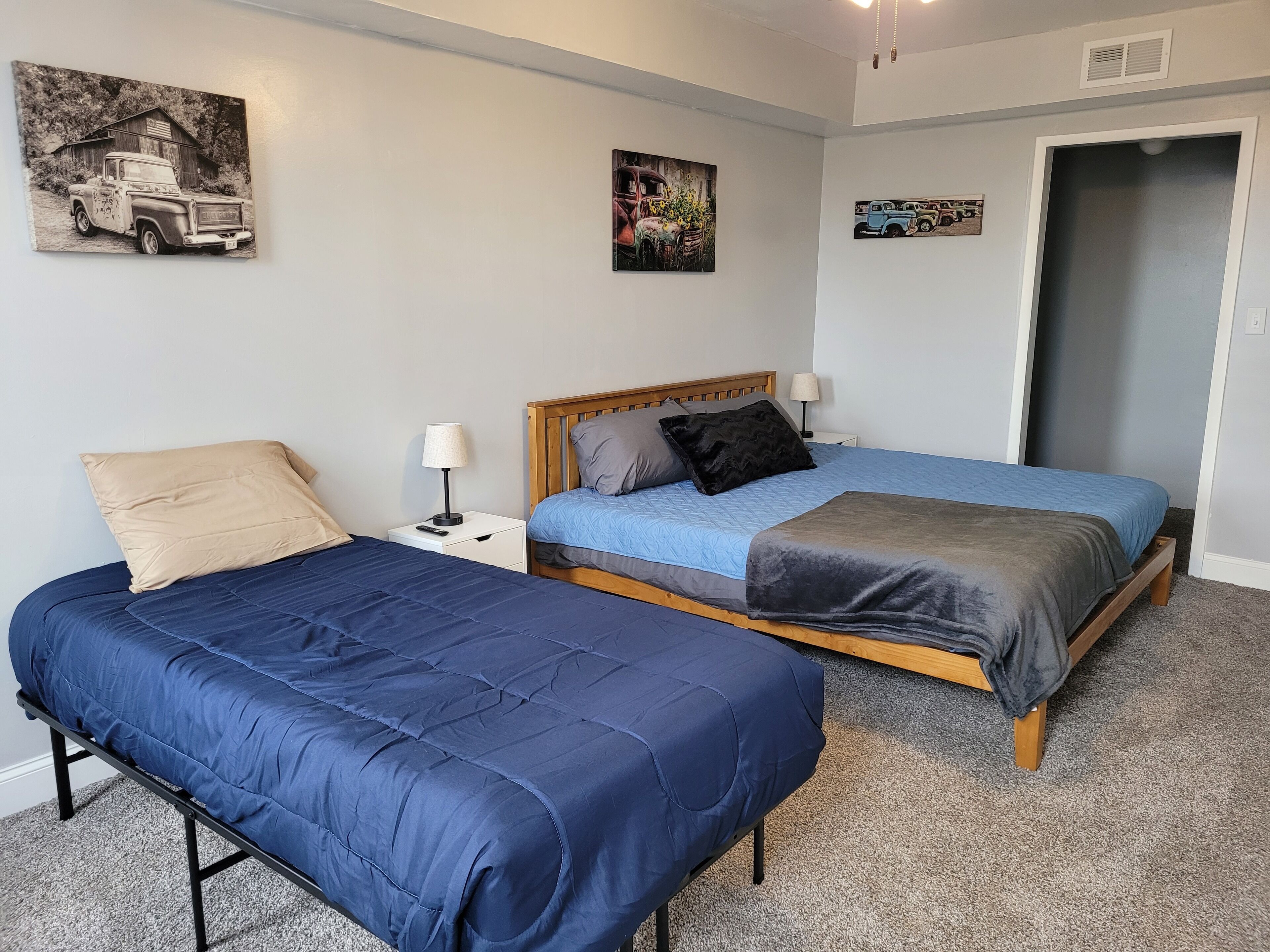 A bedroom with two beds, a wooden headboard, a nightstand with a lamp, and wall art.