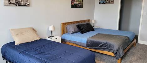 A bedroom with two beds, a wooden headboard, a nightstand with a lamp, and wall art.