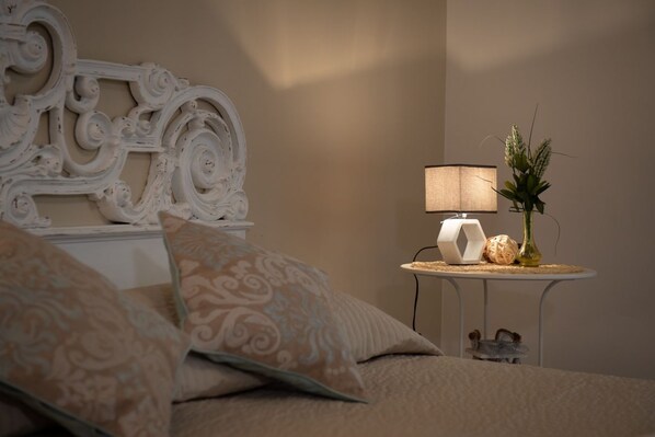 A bedroom with a bed, decorative headboard, bedside table with a lamp, and a vase with flowers. - House Bonifacio VIII (Roma)
