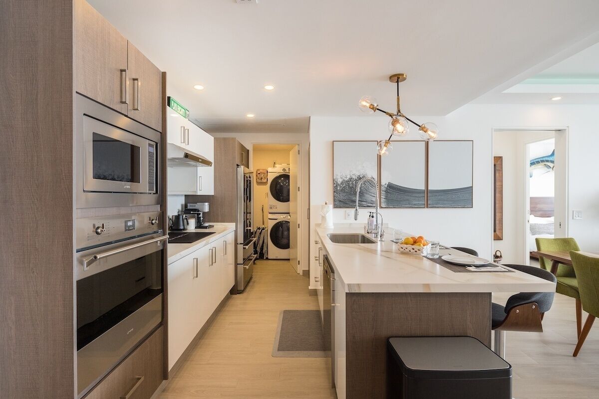 A modern kitchen with stainless steel appliances, a central island, and a view into the laundry area.