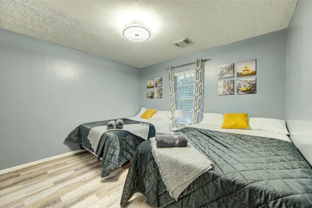 Een slaapkamer met twee bedden, een raam met zonwering, een plafondlamp en wanddecoratie.