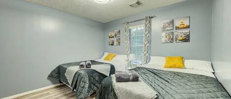Een slaapkamer met twee bedden, een raam met zonwering, een plafondlamp en wanddecoratie.