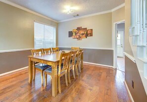 A dining room with a wooden table and chairs, a painting on the wall, and a window with blinds. - Comfortable, Upscale House with a pool and spa! (Katy)