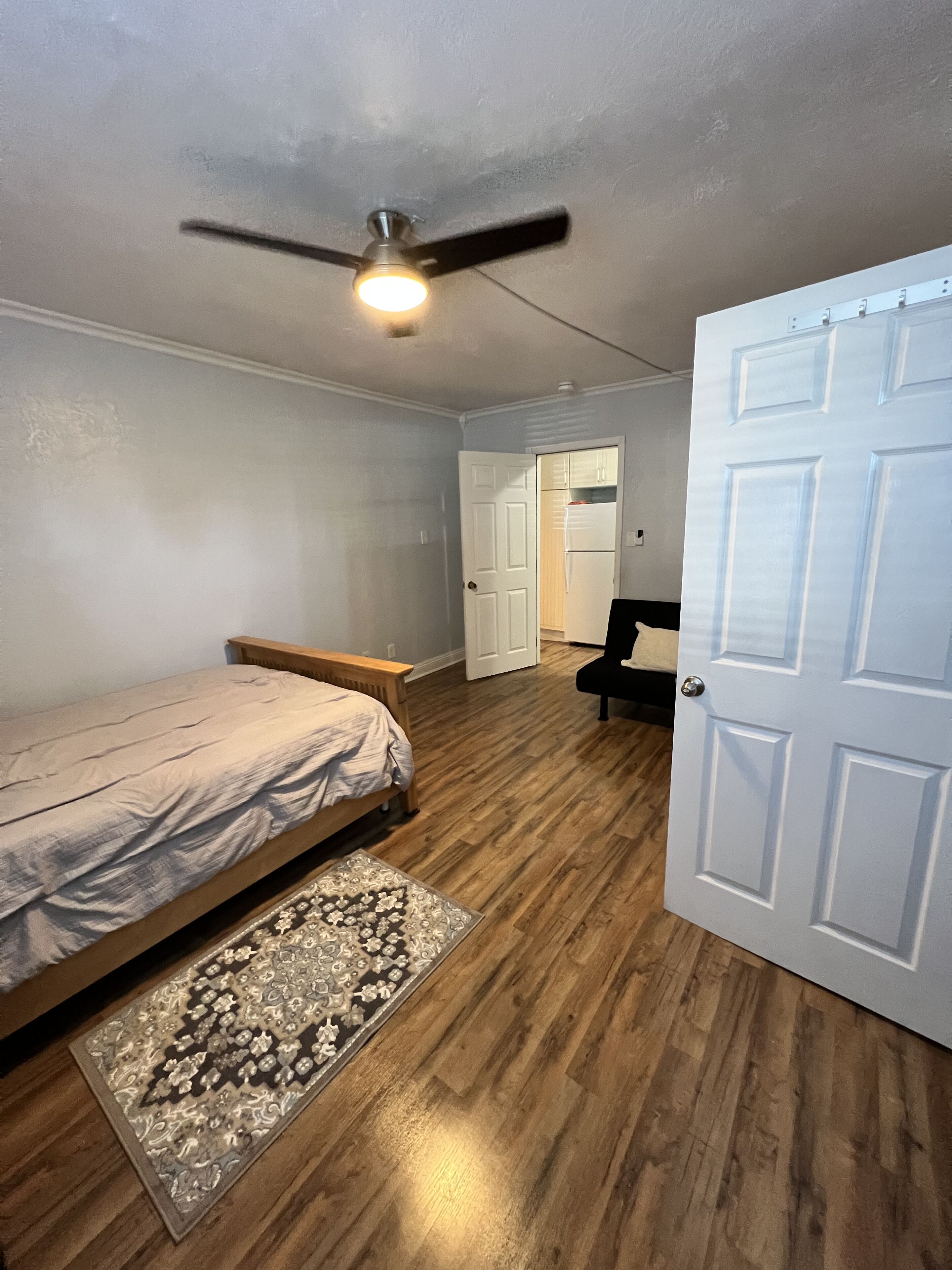 Une chambre à coucher avec un lit, un ventilateur de plafond, une porte et un tapis.