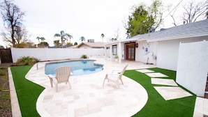 Un patio trasero con piscina, dos sillas de jardín y una zona de patio con diseño de mosaico de espiga.