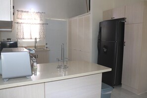 Compact kitchen with a stainless steel refrigerator, sink, and light-colored cabinetry.