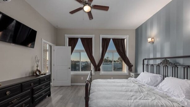Une chambre à coucher comprenant un lit, une commode, un ventilateur de plafond et un téléviseur fixé au mur.