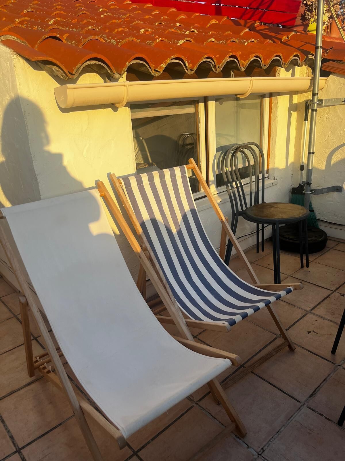 A patio with two striped lounge chairs, a table, and a red umbrella.