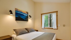 A bedroom with a bed, two bedside tables, a painting, a window with curtains, and a nightstand. - Hanging Rock Cabin - (Lyndhurst)