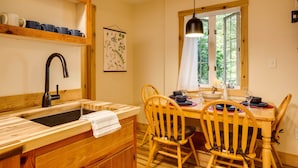 A kitchen with a wooden table, chairs, and a window with a view of greenery. - Hanging Rock Cabin - (Lyndhurst)