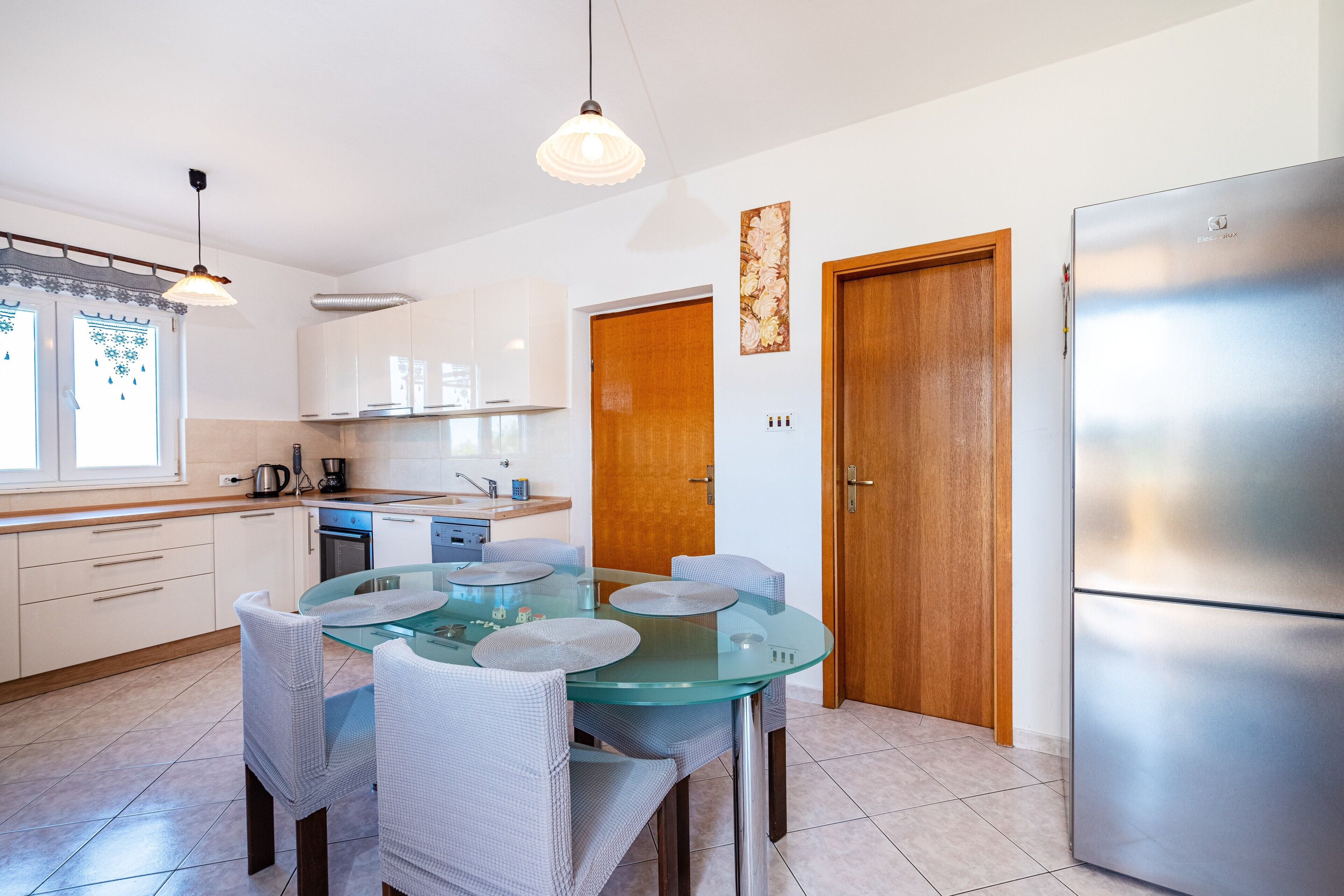 A modern kitchen with white cabinets, a glass dining table, and a stainless steel refrigerator.
