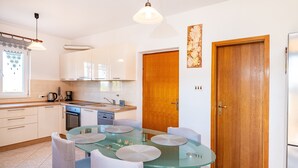 A modern kitchen with white cabinets, a glass dining table, and a wooden door. - Apartments Milena - One Bedroom Apartment with  Sea View (Novigrad - Zadar)
