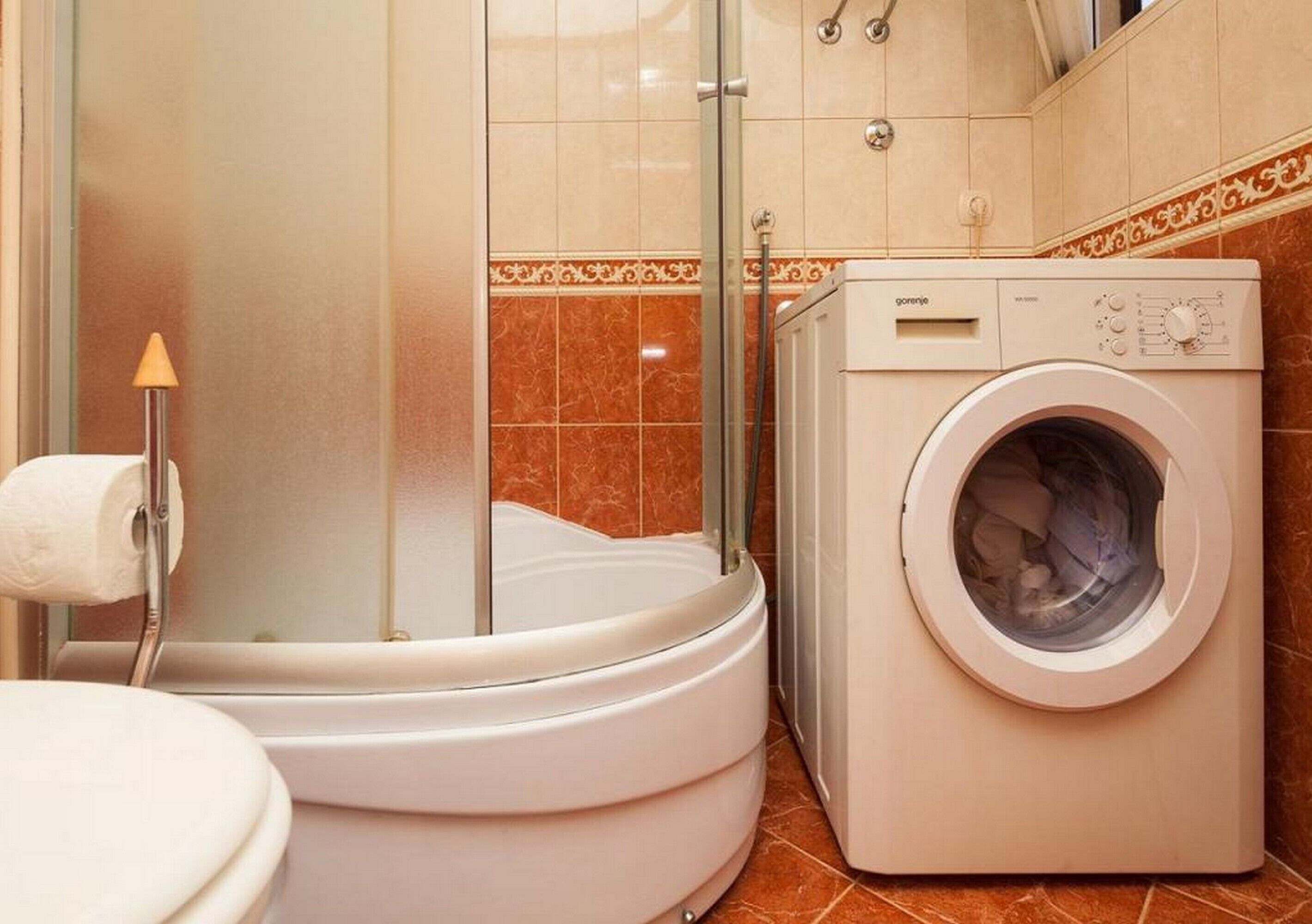 A compact bathroom with a shower, toilet, and a front-loading washing machine.