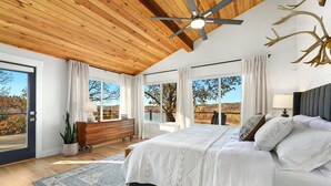 Een slaapkamer met een groot bed, houten plafond en uitzicht op de omgeving.