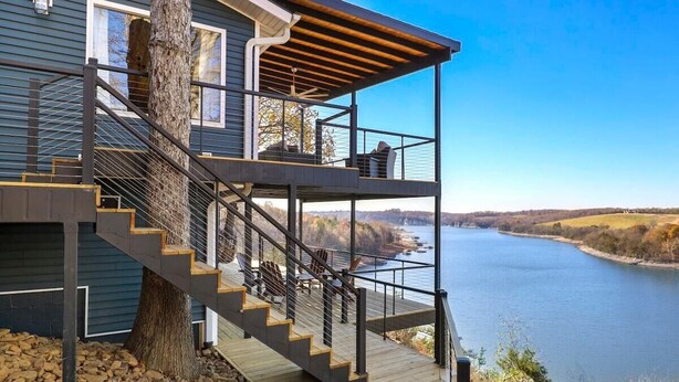 Een modern huis met een houten terras, een trap naar een balkon en uitzicht op een rivier.