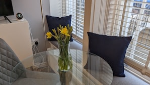 A modern living room with a glass-top coffee table, a grey sofa, and a vase of yellow flowers. - Stylish 1 Bed Apartment with Sea views (Shanklin)