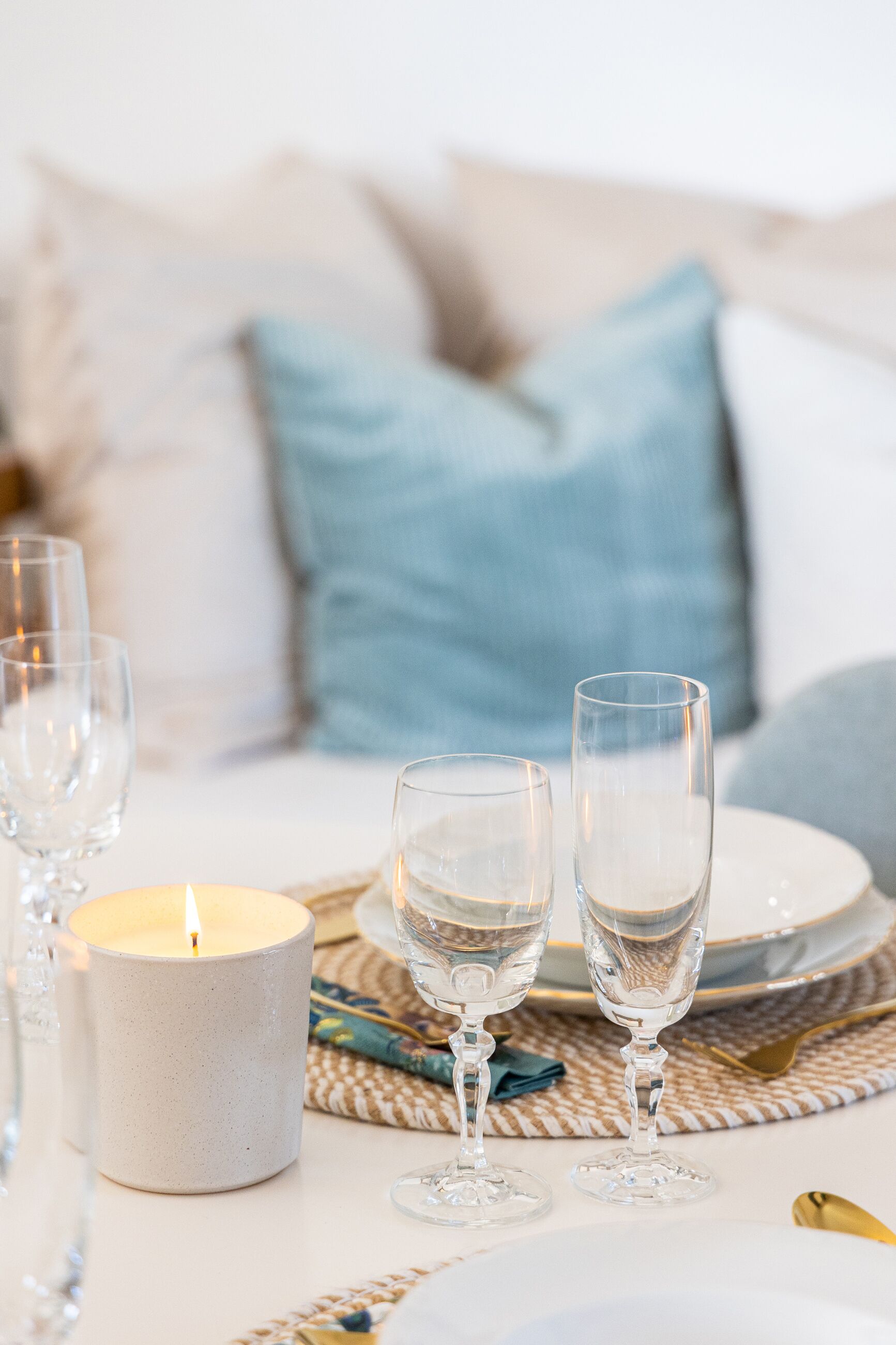 Une bougie, deux verres à vin et une assiette sur une table recouverte d’un set de table en fibres tressées.