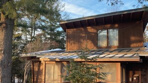A wooden cabin with a sloped roof, large windows, and a wooden deck.