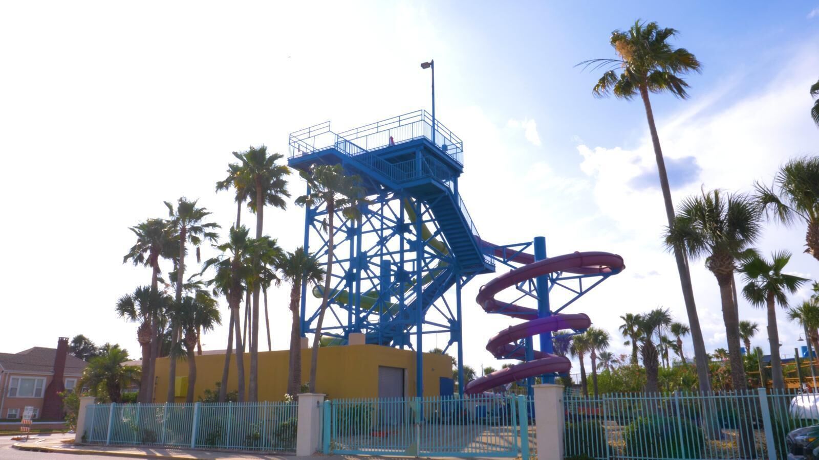 Een waterpark met een blauwe spiraal glijbaan en een geel gebouw op de achtergrond.