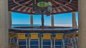 A covered outdoor bar area with a view of the sea, featuring a central bar and yellow chairs.