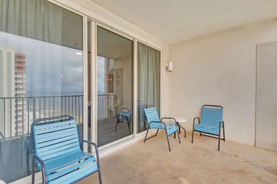A balcony with blue metal chairs and a glass door leading to an interior space.