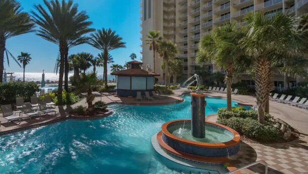 A hotel pool area with a hot tub, palm trees, and a view of the ocean.