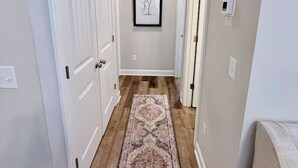 A hallway with white doors, a framed picture on the wall, and a patterned rug on the floor. - Budget Friendly Bungalow (Raleigh)