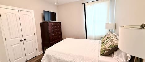 A bedroom with a bed, a dresser, a ceiling fan, a TV, and a window with curtains.