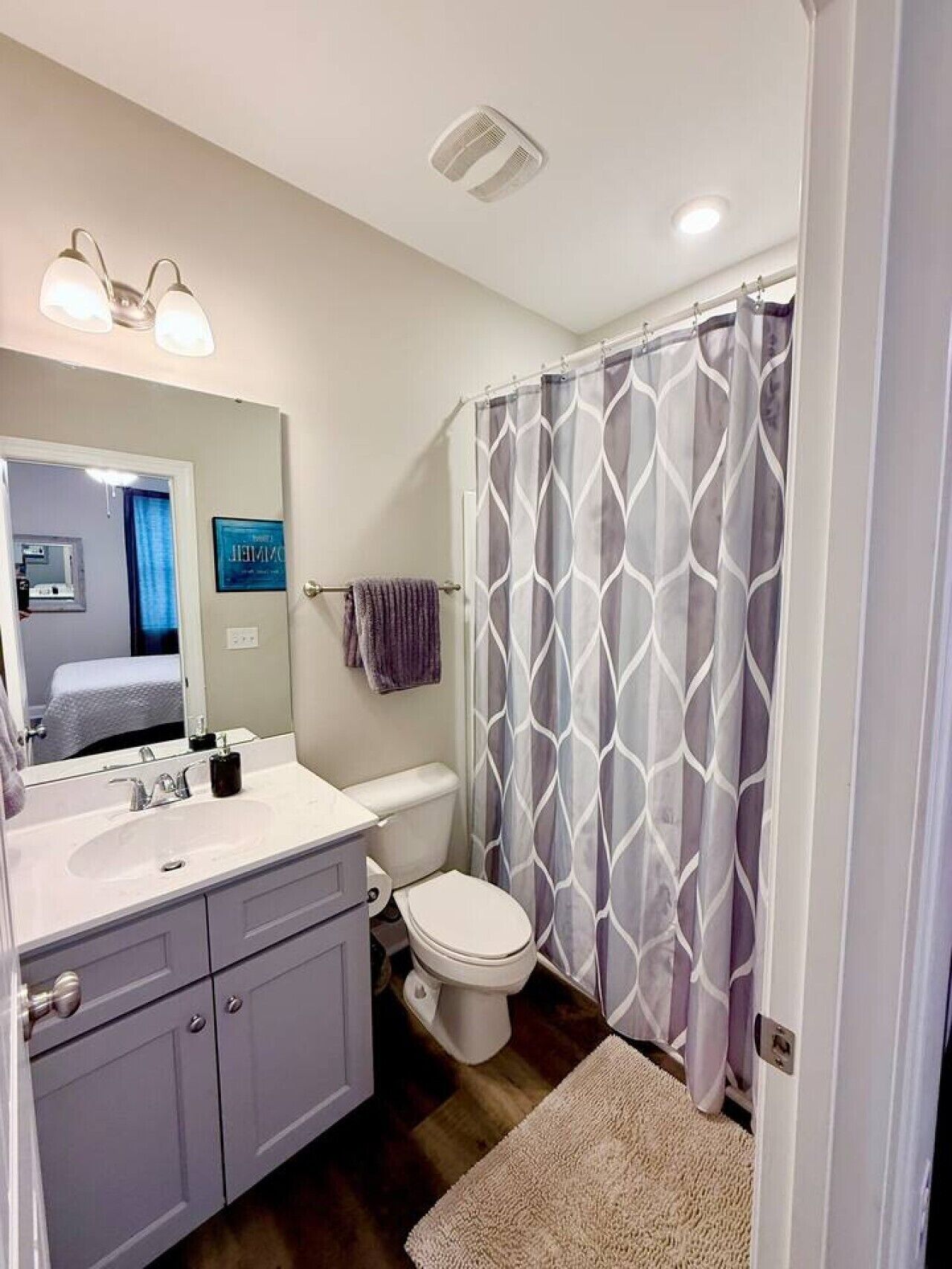 A bathroom with a white sink, a toilet, a shower curtain with a geometric pattern, and a mirror above the sink.