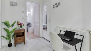Una habitación moderna con una computadora portátil sobre una mesa, una planta en maceta y una silla blanca.