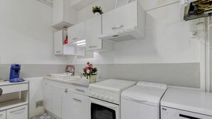 Cocina moderna con armarios blancos, horno empotrado, cafetera y un lavabo.