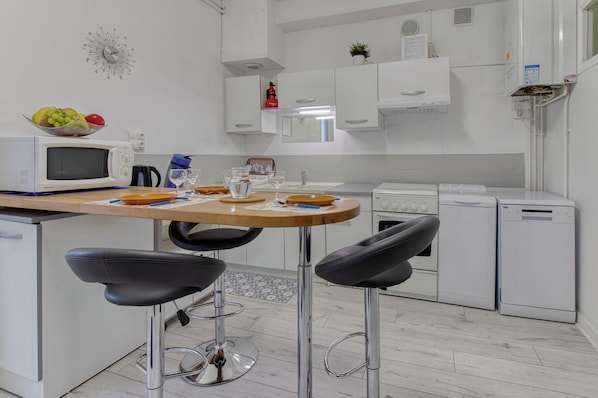 A modern kitchen with a microwave, sink, and dishwasher. There are two bar stools and a wooden table.