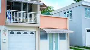 A two-story residential building with a white garage door, a balcony with a white railing, and a small awning over the entrance. - Lovalier Luxury Studio (Fajardo)