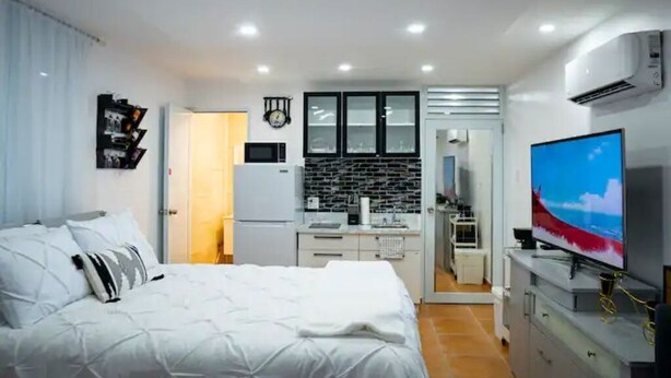 A modern bedroom with a large bed, a television, and a kitchenette in the background. - Lovalier Luxury Studio (Fajardo)