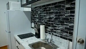 A compact kitchen with a black and white tiled backsplash, a stainless steel sink, and a built-in microwave. - Lovalier Luxury Studio (Fajardo)